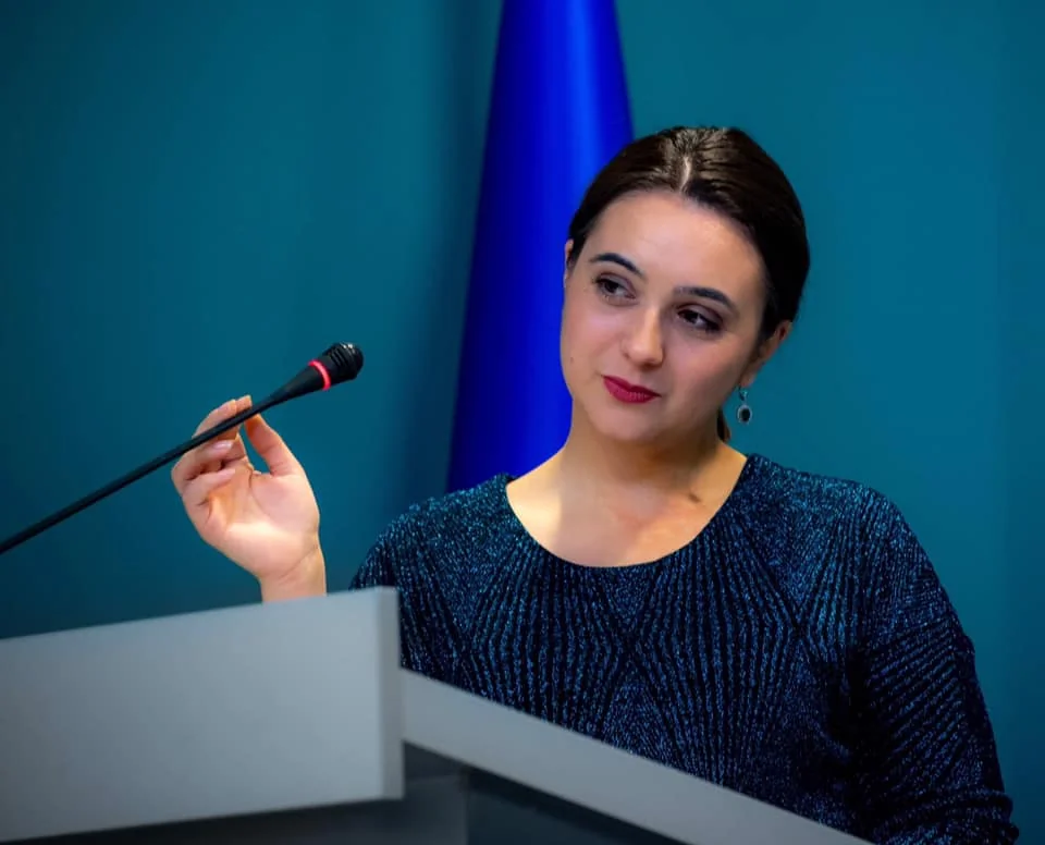 Юлія Мендель виступає за трибуною на тлі прапора України