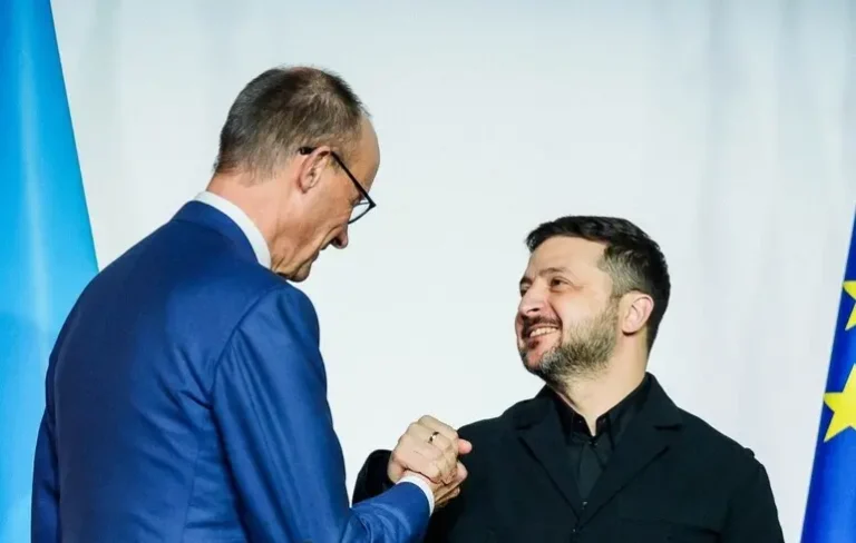 Канцлер Фридрих Мерц и президент Зеленский жмут руки на фоне флагов Украины и ЕС