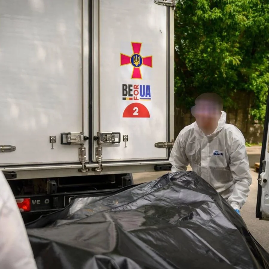 Працівник у захисному костюмі біля вантажівки з тілами загиблих захисників України