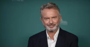 Сем Нілл, актор «Парку Юрського періоду» у темному костюмі