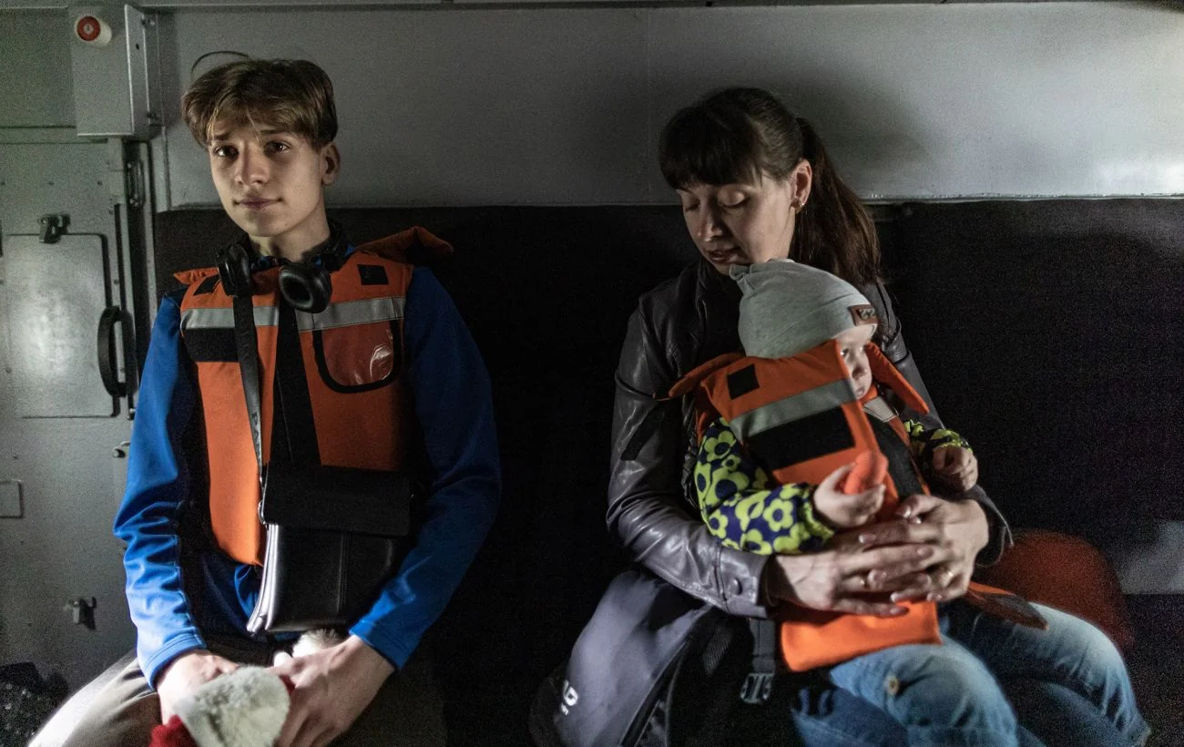 Підліток і жінка з немовлям у рятувальних жилетах у транспорті
