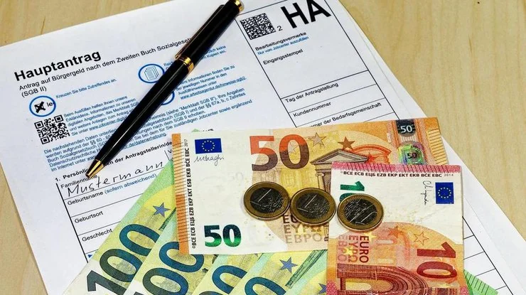 Заявление на Bürgergeld с банкнотами евро и ручкой для заполнения