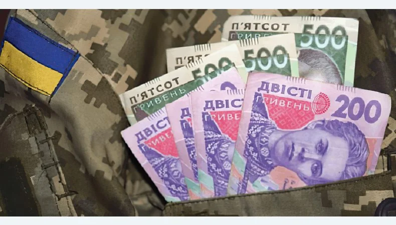Банкноти гривень у кишені військової форми з прапором України
