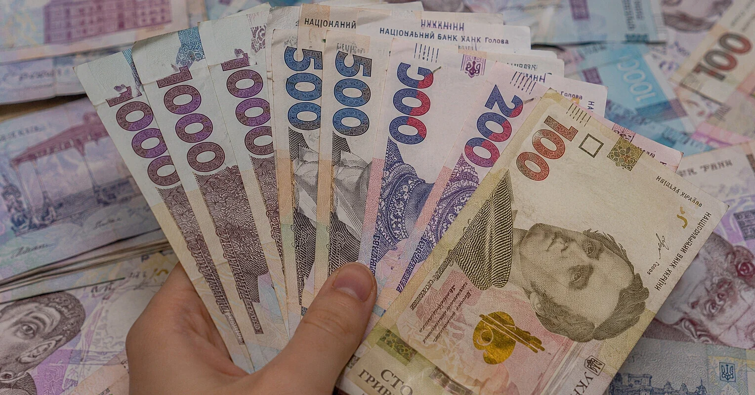 Рука держит банкноты украинской гривны номиналом 100–1000