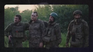 Чотири бійці в камуфляжі та бронежилетах стоять у полі на тлі дерев увечері