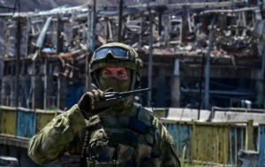 Військовий у камуфляжі з рацією на тлі зруйнованої будівлі