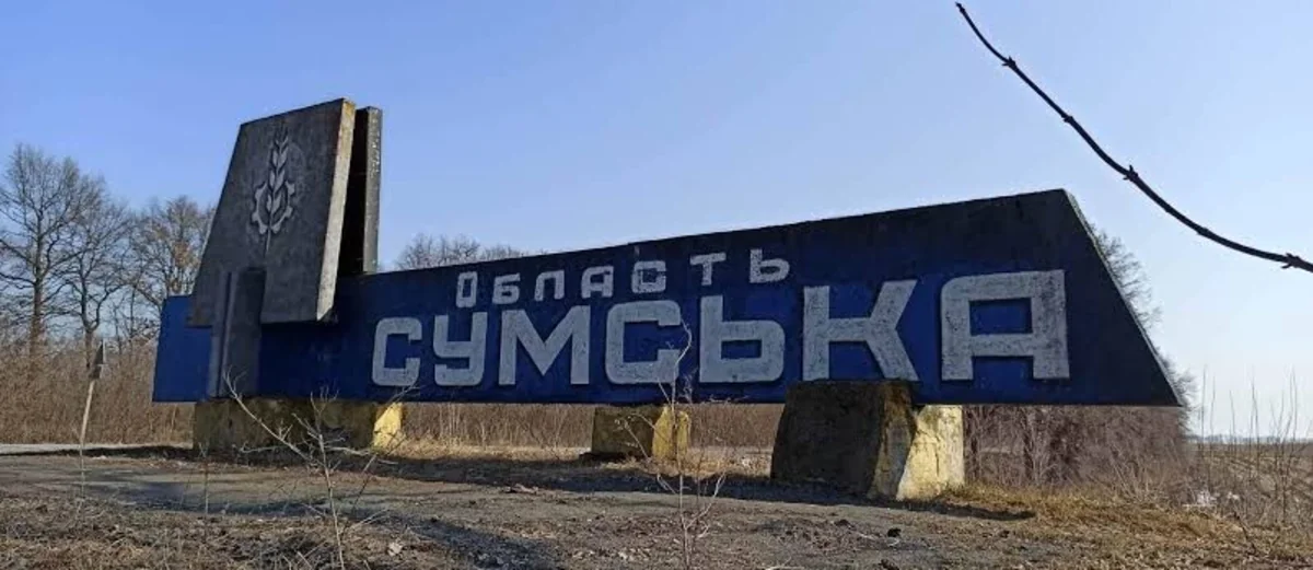 Синя стела з написом Область Сумська стоїть біля дороги серед сухої трави