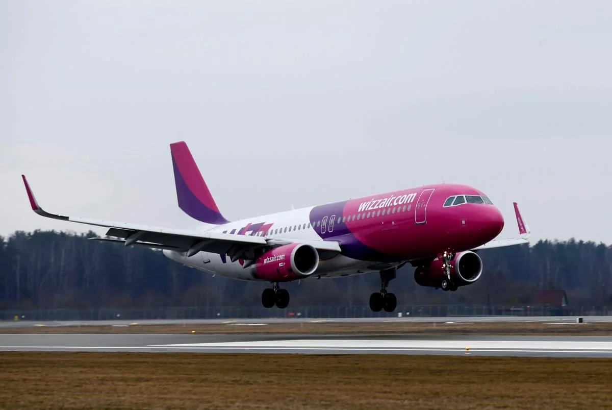 Рожево-білий літак Wizz Air злітає зі смуги під сірим небом
